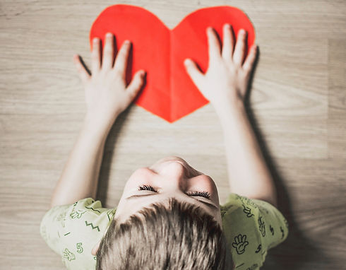 boy in green shirt holding red paper heart cutout on brown table_edited.jpg