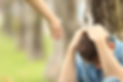 Sad teen sitting on the grass in a park and a woman hand offering help