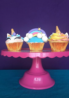 3 cupcakes on a cake drum, cupcake 1 and 3 are designed like a unicorn and cupcake 2 is designed with a rainbow and clouds. All designed in fondant
