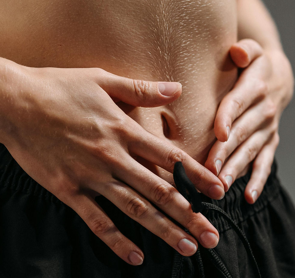 Person holding their stomach with both hands, showing discomfort. Skin is pale; wearing black shorts. Close-up, neutral background.