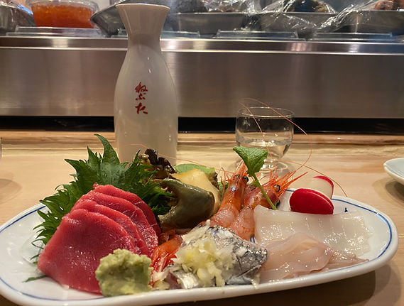 Fresh sashimi plate with wasabi and ginger, and a sake bottle and glass in the background, 