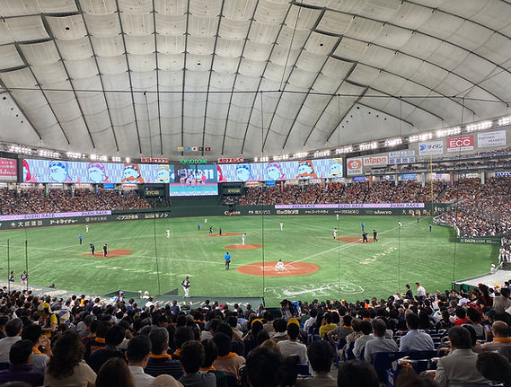 A baseball game being played at Tokyo Dome with the scoreboard lit up in the background