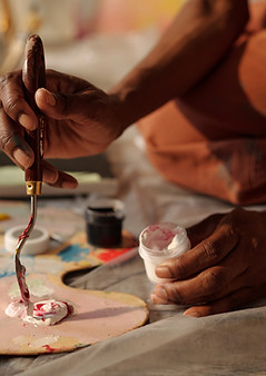 Hands skillfully holding palette knife and mixing paints on canvas. Background reveals art
