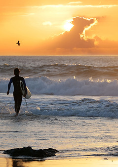SILHOUETTE_ Surfer walking into the water holding surfboard to catch the last waves before