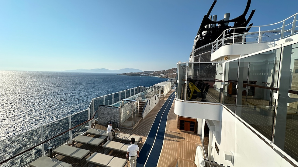 Open deck of a luxury cruise ship overlooking the sea and a coastal destination in calm, sunny weather.