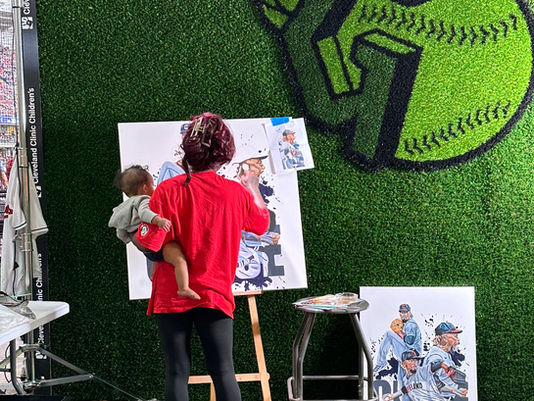 Stina Aleah painting live at the Cleveland Guardians game with her infant on her hip.