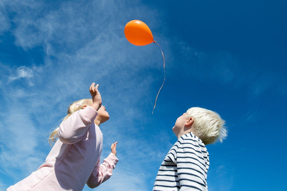 Two children releasing a balloon into the air.