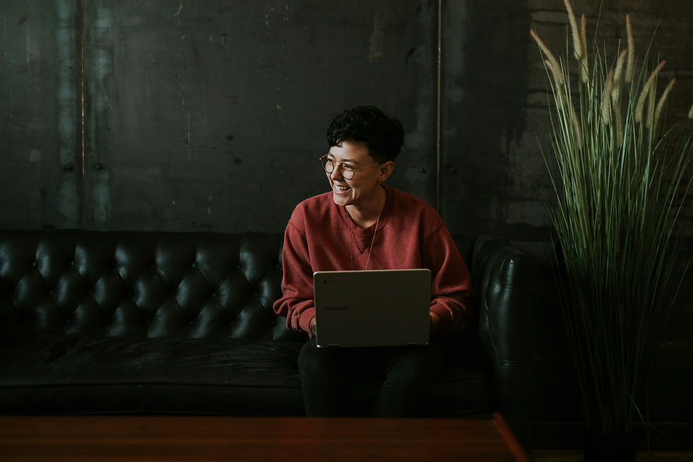 Smiling man using laptop while sitting on black leather couch with a plant beside