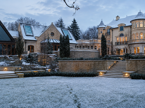 Snow-dusted terraced stone garden with lit staircases at dusk beside a limestone chateau estate in Toronto