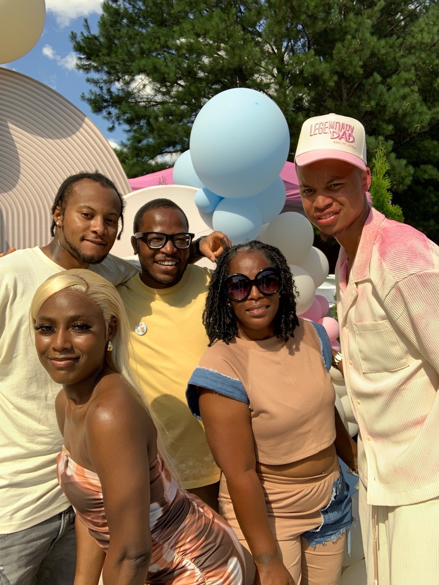 Friends posing at an outdoor baby shower photo booth with a balloon arch