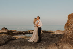 Brudpar står och myser tillsammans vid vattnet samtidigt som två svanar glider förbi
