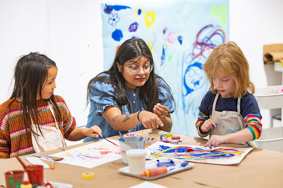 An adult and two young children sit together at a table, painting and making crafts.
