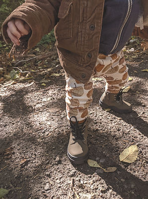 photo of the bottom half of a child walking through leaves, with pumpkin leggings and green combat boots on