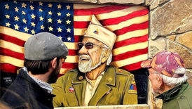 Mike Sekletar showing a painted portrait of a veteran in front of an American flag mural.