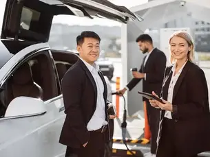 Ein Mann und eine Frau lachen vor einem E-Auto, das gerade lädt, in die Kamera