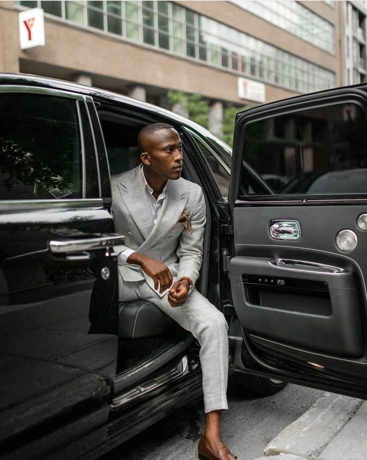 Confident, well-dressed man stepping out of a luxury black car in a tailored grey suit, representing success, status, and ambition