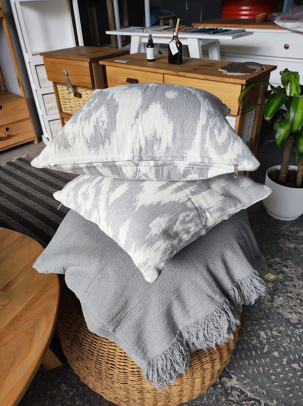 Miniatura: Pila de cojines decorativos y manta sobre taburete tejido