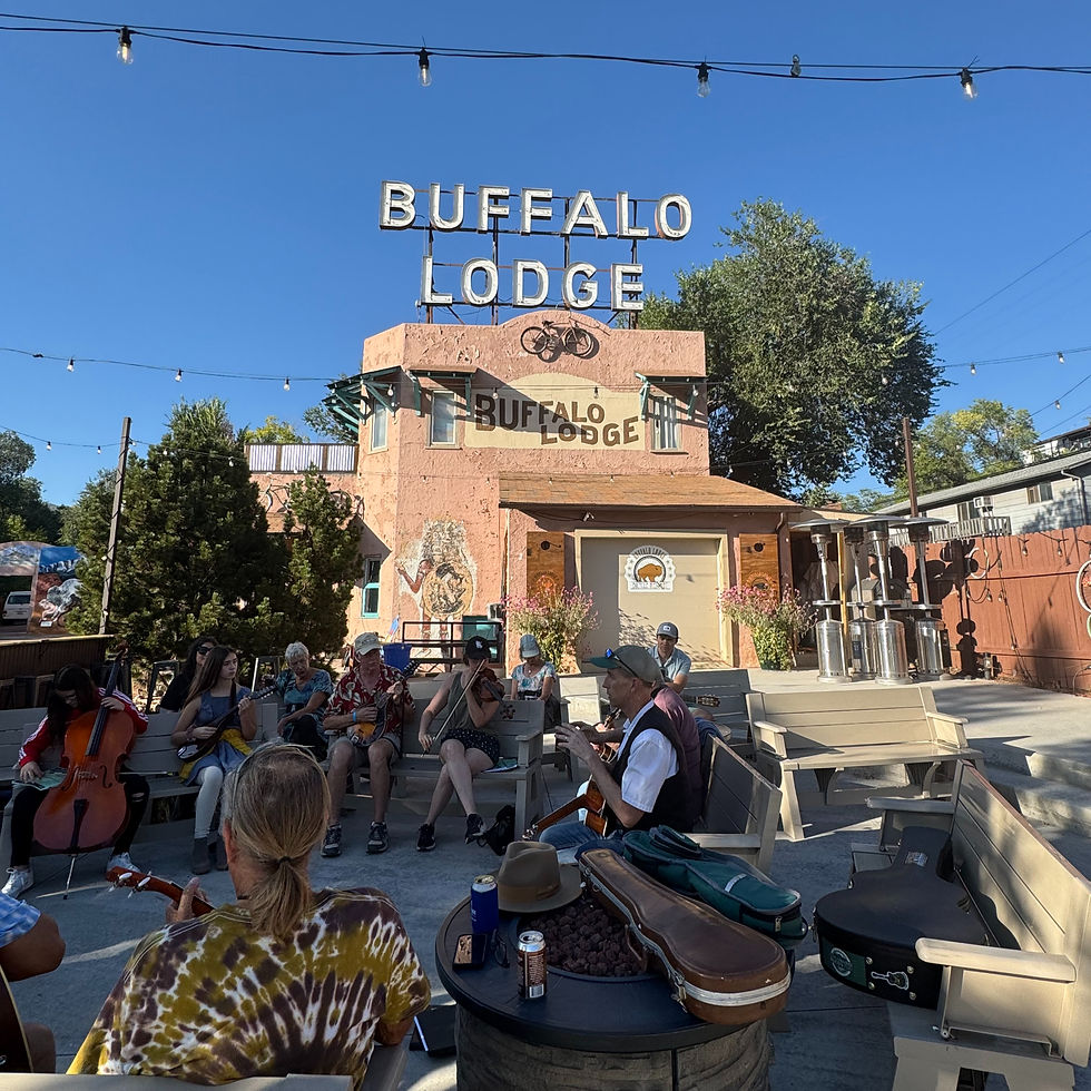 Group of musicians sitting in front of the Buffalo Lodge on a clear blue sky day.