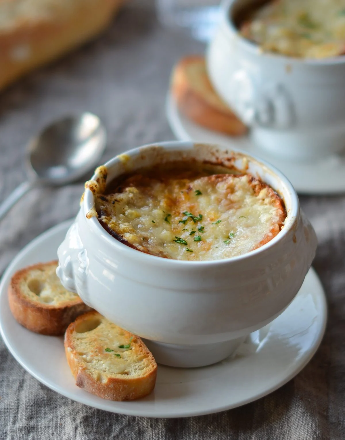Bowl of French Onion Soup on a plate with 2 slices of bread on the side.
