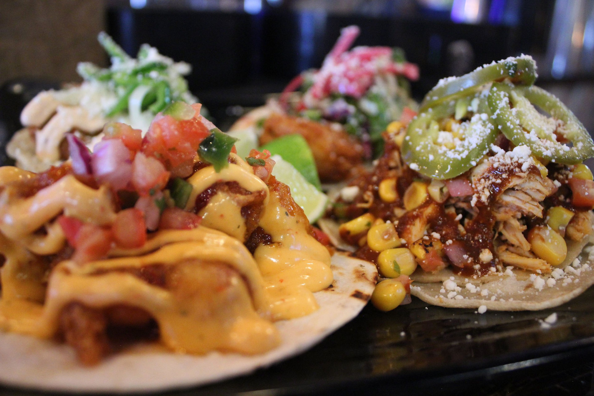 Photo of 4 different street tacos on a plate with a variety of toppings.