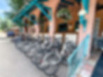 Bright sunny day, several bikes lined up at a bike rack in front of the Buffalo Lodge with flowers hanging in the archways.