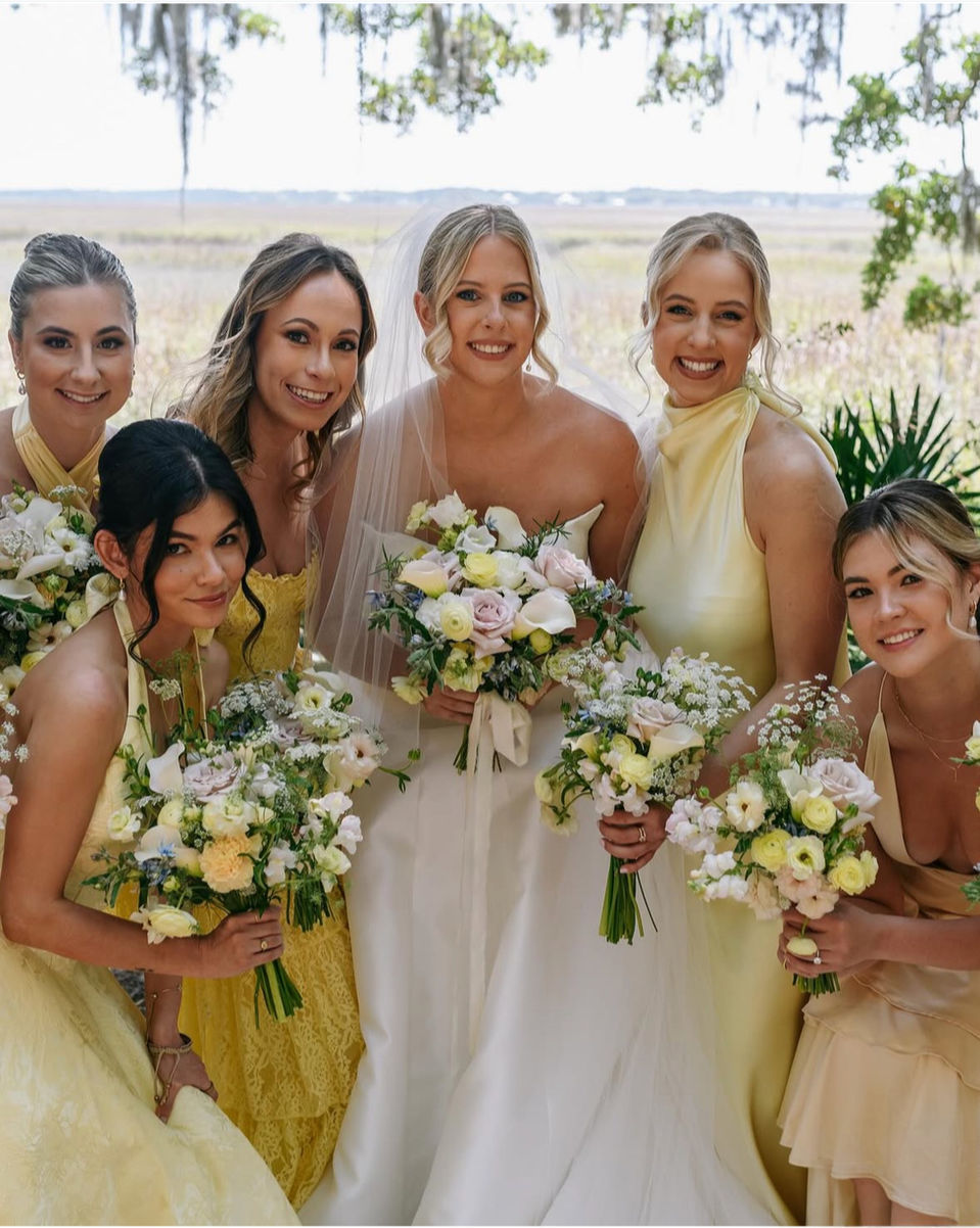 Bride with bridesmaids in butter yellow dresses holding white and blush bouquets under Spanish moss at an April wedding at Walker’s Landing.