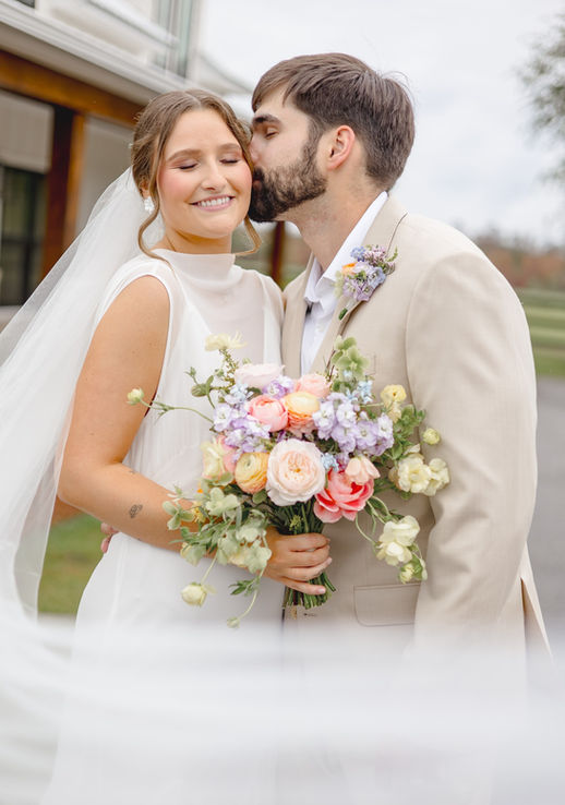Newlyweds embracing with a pastel spring bouquet featuring garden roses, ranunculus and seasonal flowers.