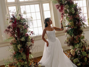 Bride in strapless gown standing between moody floral towers at Karpeles Grand, featuring American grown flowers in a sustainable ceremony installation.