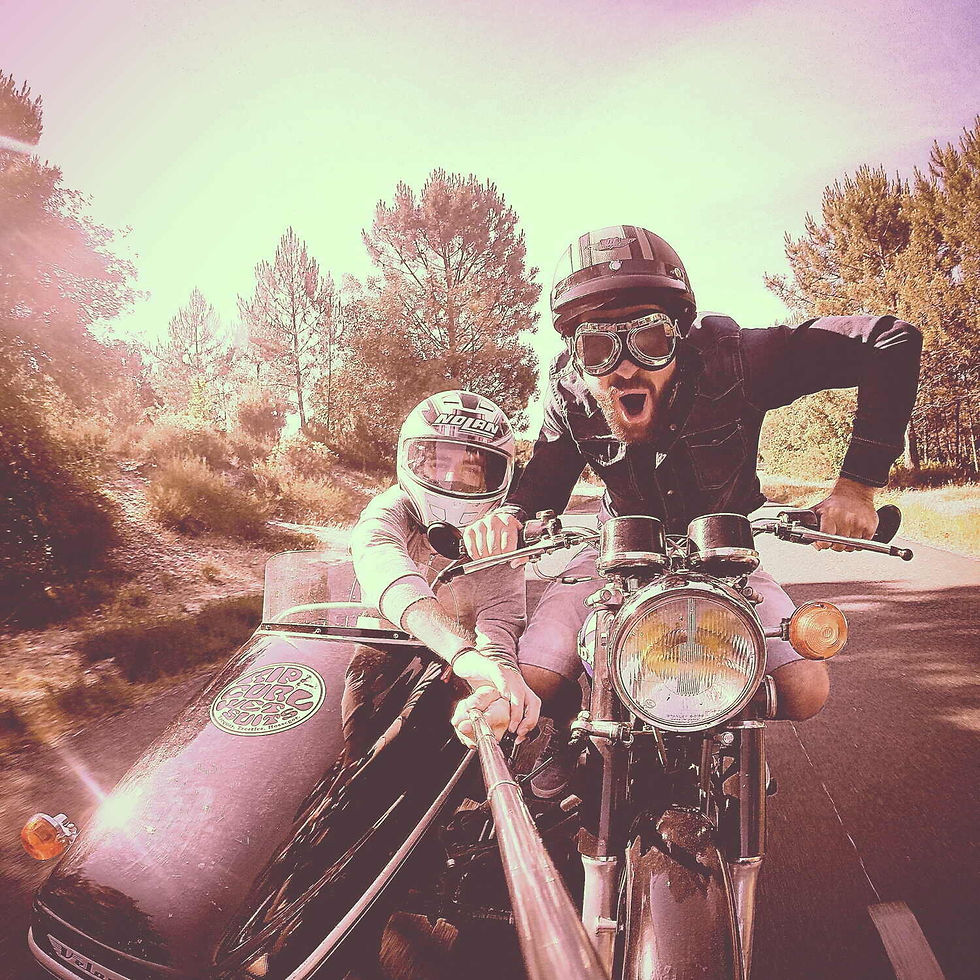 Two people on a motorcycle with a sidecar take a selfie on a sunny road