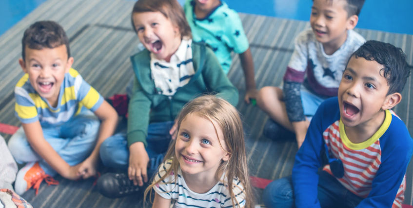 Young school children sitting on the floor smiling and laughing