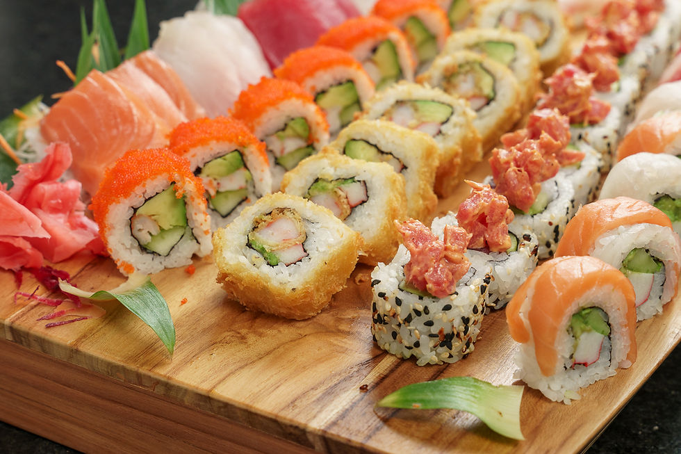 Surtido de sushi sobre tabla de madera, incluye nigiri y rollos con salmón, aguacate y huevas naranjas. Fondo negro, ambiente fresco.
