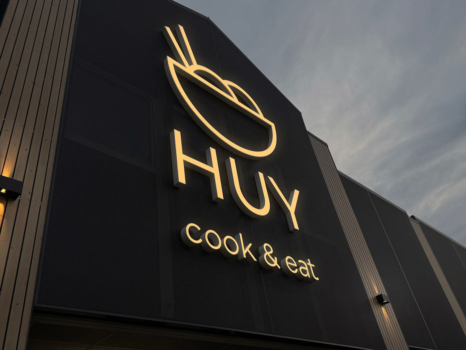 Beleuchtete HUY 3D Buchstaben und Logo auf dunkler Gebäudefassade