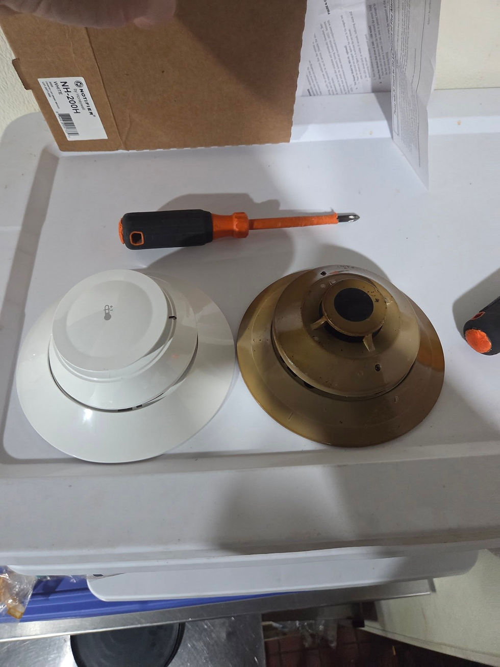 Old fire alarm detector removed from a Connecticut restaurant kitchen showing heavy grease buildup alongside the new replacement device.