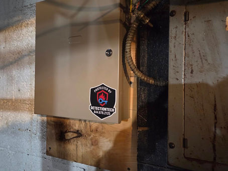 Gray metal box with a padlock on a textured wall. A sticker reads "Protected by DetectionTech 844.676.2125" with a red flame and blue key logo.