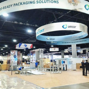 Rollable vinyl flooring installed in a large trade show exhibit booth with overhead signage and branded display areas.