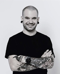 A young man with tattoos stands with his arms crossed