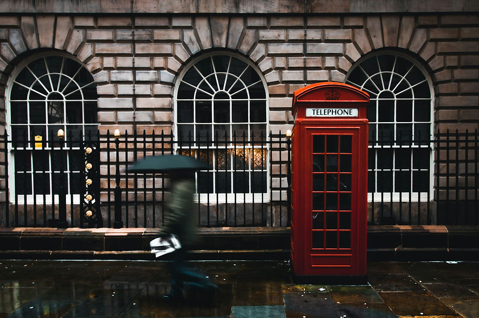 A red phone booth on a rainy street with a person in motion blur walking by