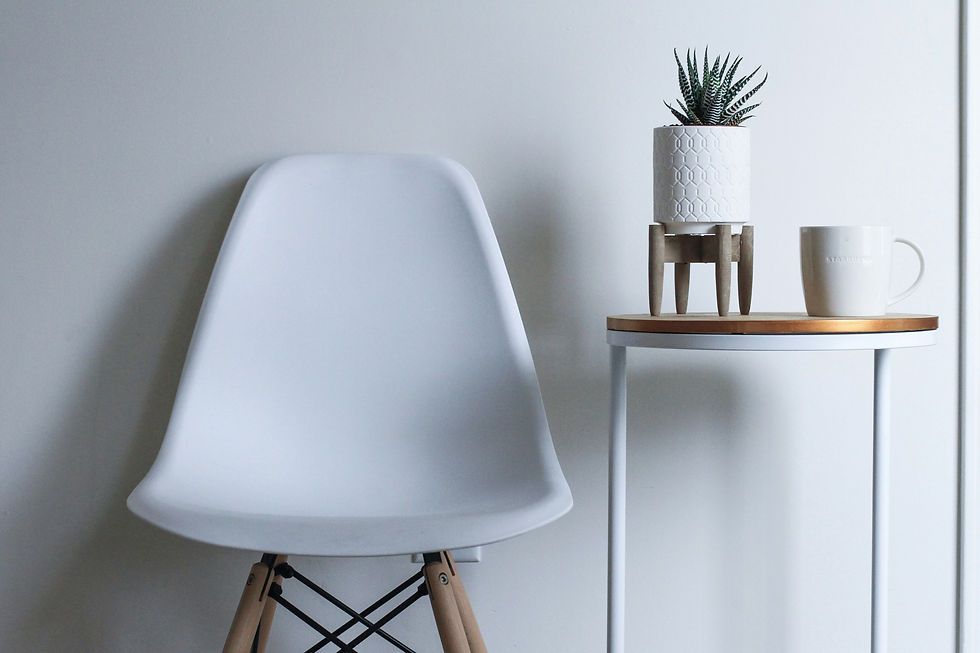 A minimalist setup featuring a white chair, a small table with a potted plant, and a coffee mug against a plain wall