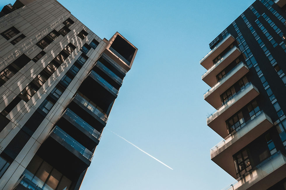 Looking up between two modern high-rise buildings to a clear blue sky with a single jet trail