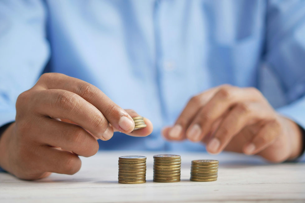 Hands stacking coins in increasing amounts on a light wooden surface.
