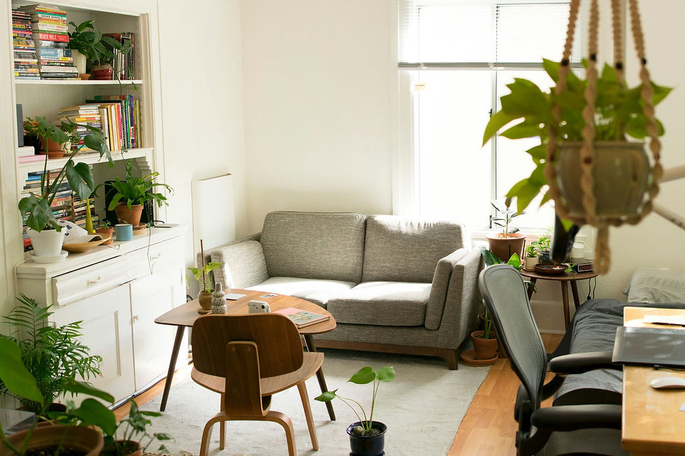 A cozy, well-lit living room with a gray sofa, wooden furniture, and an array of green plants, creating a serene and inviting atmosphere