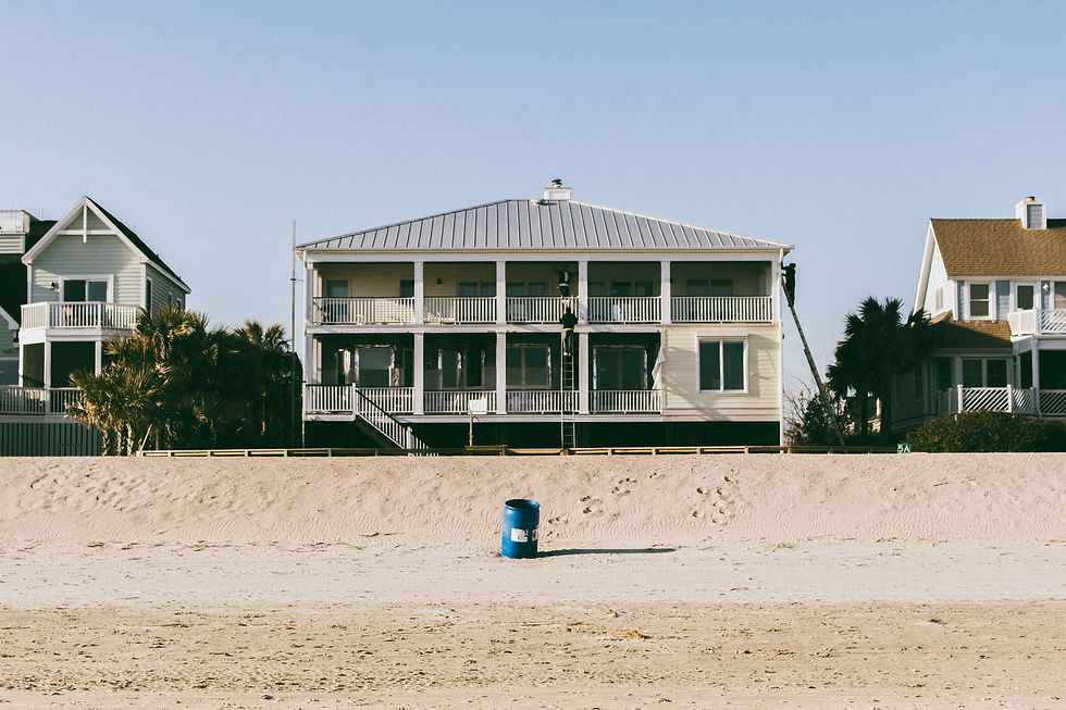 Beachfront homes with balconies overlooking a sandy shore, set against a clear, sunny sky.