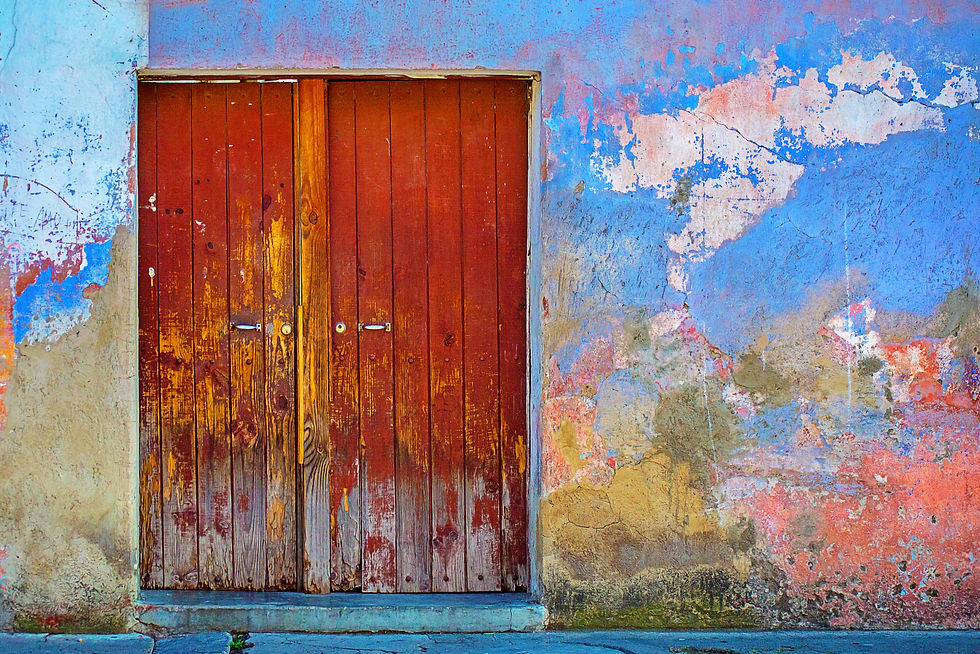 A weathered wooden door set in a colorful, textured wall with peeling blue, pink, and beige paint in a rustic style