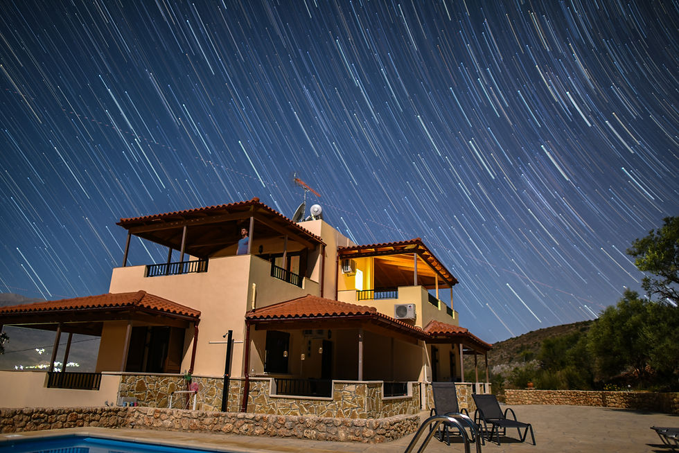 Long exposure night photo of a house with star trails in the sky, surrounded by a patio and a swimming pool in the foreground