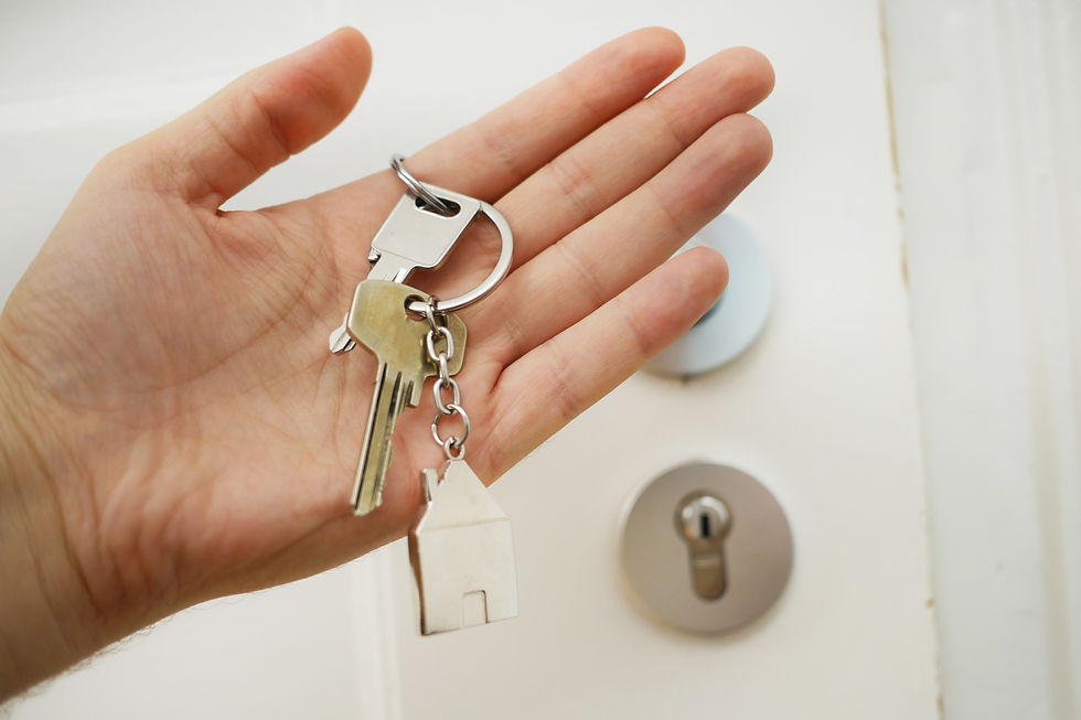 Hand holding key with house keychain, door lock in background