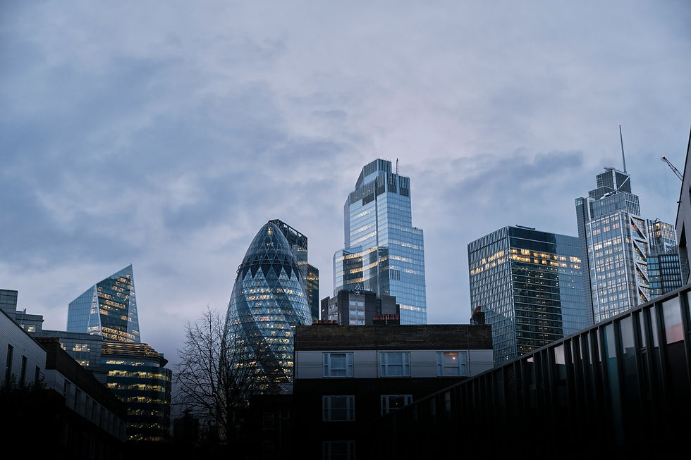 A twilight cityscape with illuminated modern buildings under a cloudy sky.