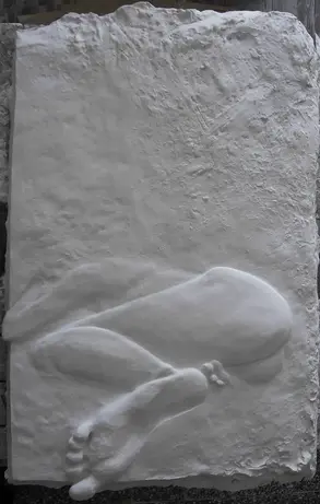 Plaster relief cast of clay sculpture showing sleeping nude woman, prominent sculpted foot gradually flattens into relief background.