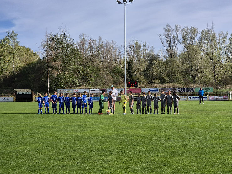 Fußballjugendmannschaften in blauen und grauen Trikots stehen sich am Spielfeld gegenüber