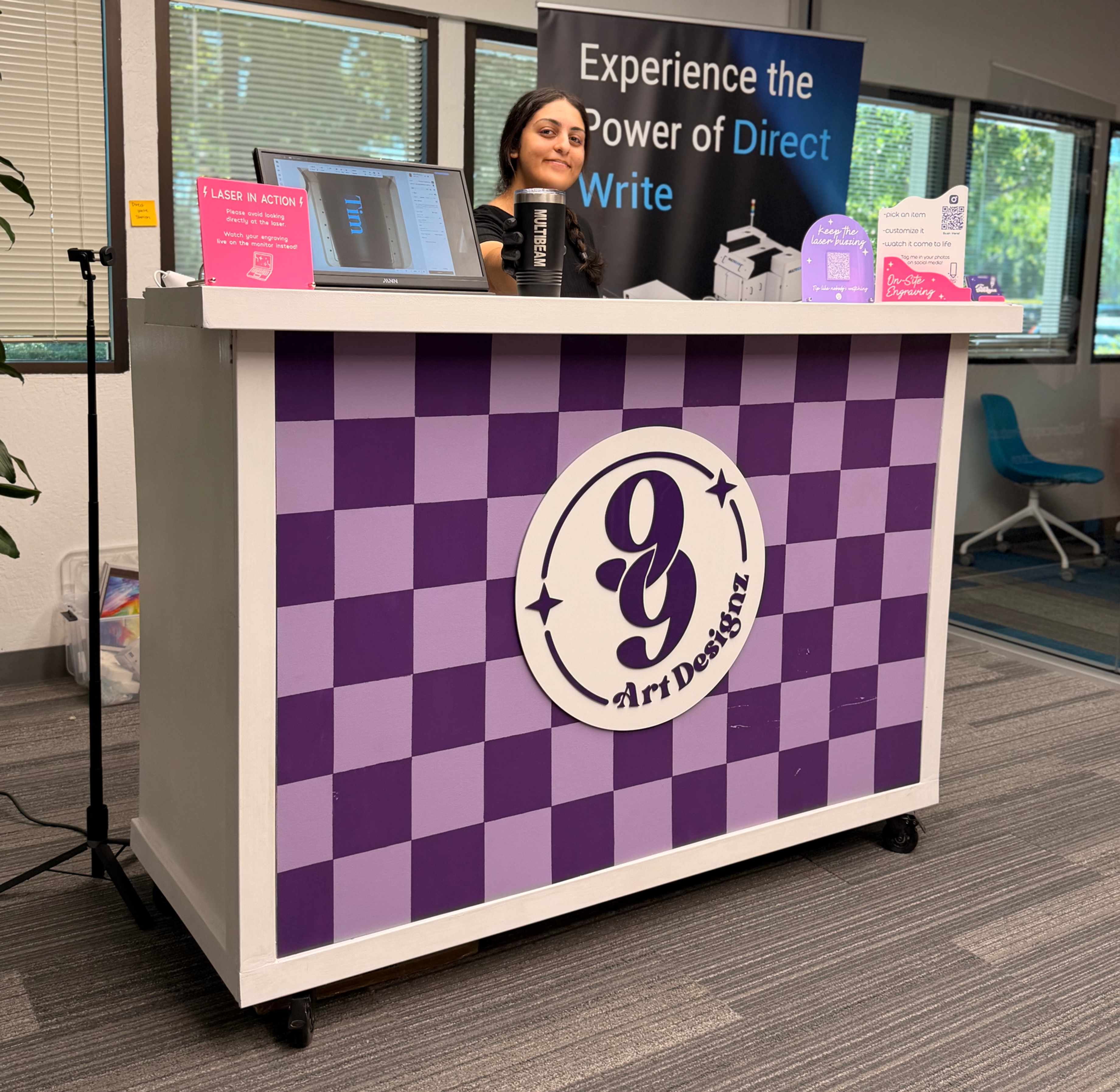 Woman smiling behind a purple 99 Art Designz wooden bar like table in an office event corporate party.