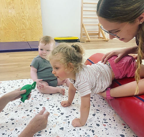 Child with disability and gross motor delay participating in paediatric physiotherapy over a therapy bolster with a trained paediatric physiotherapist